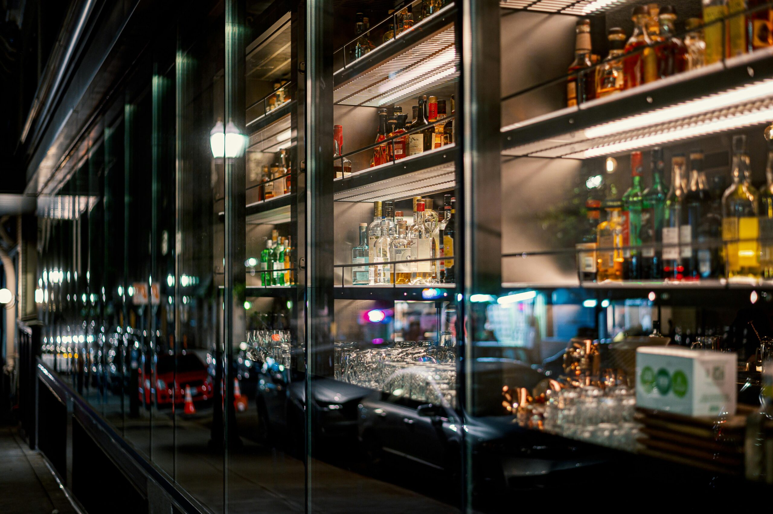 Bar shelves with a variety of liquor bottles and reflections of street lights at night.